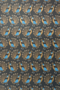 A roll of fabric with a repeating peacock pattern on a dark charcoal background. The peacocks are detailed in gold and bright blue.